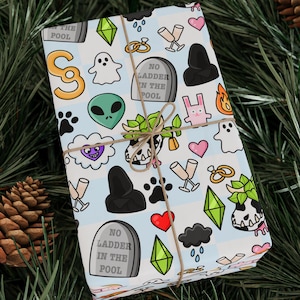 Puede incluir: Papel de regalo blanco con un patrón repetitivo de imágenes de dibujos animados coloridos, que incluyen un fantasma, un extraterrestre, una huella de pata, un corazón y una lápida que dice "No hay escalera en la piscina".