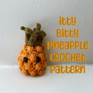 Pode incluir: Um brinquedo de abacaxi de crochê com o topo verde e o corpo laranja. O brinquedo tem olhos pretos e uma expressão fofa. O texto "itty Bitty Pineapple Crochet Pattern" está escrito em letras laranja sobre um fundo branco.