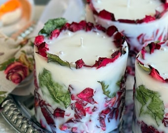 May include: Three white candles with dried rose petals and green leaves embedded in the wax. The candles are on a silver tray.
