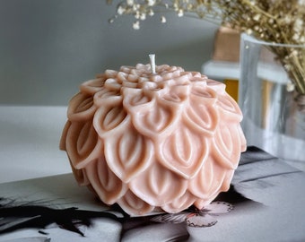 May include: A pale pink candle shaped like a flower with many petals. The candle is sitting on a book with a butterfly design.