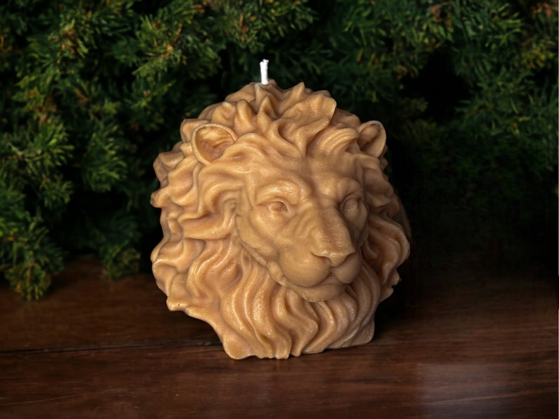 May include: A hand-crafted beeswax candle shaped like a lion's head. The candle is a light brown color and has intricate details, including the lion's mane, eyes, and nose.