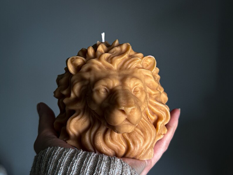 May include: A hand holds a brown beeswax candle shaped like a lion's head. The candle has a white wick.