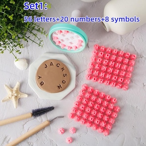 Puede incluir: Un juego de manualidades con sellos de letras y números rosas, un sello redondo y herramientas. El juego incluye 56 letras, 20 números y 8 símbolos. El texto "Set1: 56 letters+20 numbers+8 symbols" es visible.