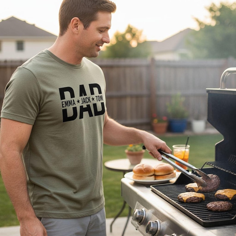 A man in a green t-shirt is grilling hamburgers and hot dogs on a barbecue grill in a backyard setting.