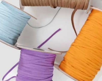 Puede incluir: Cuatro carretes de cinta de colores, incluyendo azul claro, morado, naranja y beige. La cinta está enrollada alrededor de carretes blancos.