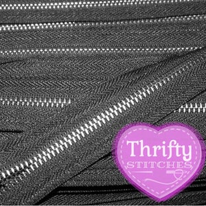 May include: Close-up of several black zippers with silver teeth. The zippers are arranged in a diagonal pattern, with the teeth of the zippers facing different directions. A purple heart-shaped logo with the text "Thrifty Stitches" is in the lower right corner.