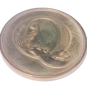 Peut inclure: Une pièce de monnaie argentée avec un grand "Q" au centre, entouré d'un motif floral sur le côté gauche. La pièce a une surface brillante et un bord en relief, d'environ 2,5 cm de diamètre.