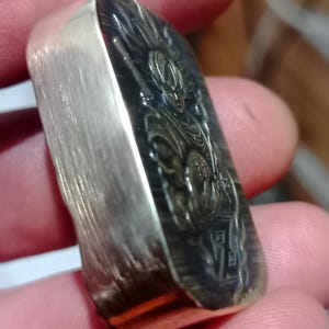 May include: A rectangular silver bar featuring an engraved image of a character with spiky hair. The bar has a brushed metal finish on the sides and a detailed design on the front.