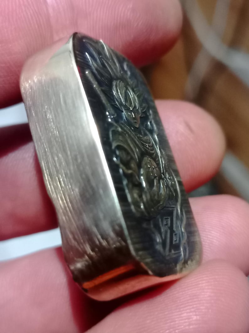 May include: A rectangular silver bar featuring an engraved image of a character with spiky hair. The bar has a brushed metal finish on the sides and a detailed design on the front.