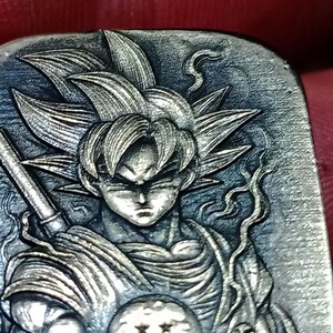 May include: A detailed, silver-toned relief carving of a character with spiky hair, holding a staff and a sphere with stars. The character's face is stern, and the artwork has intricate details.