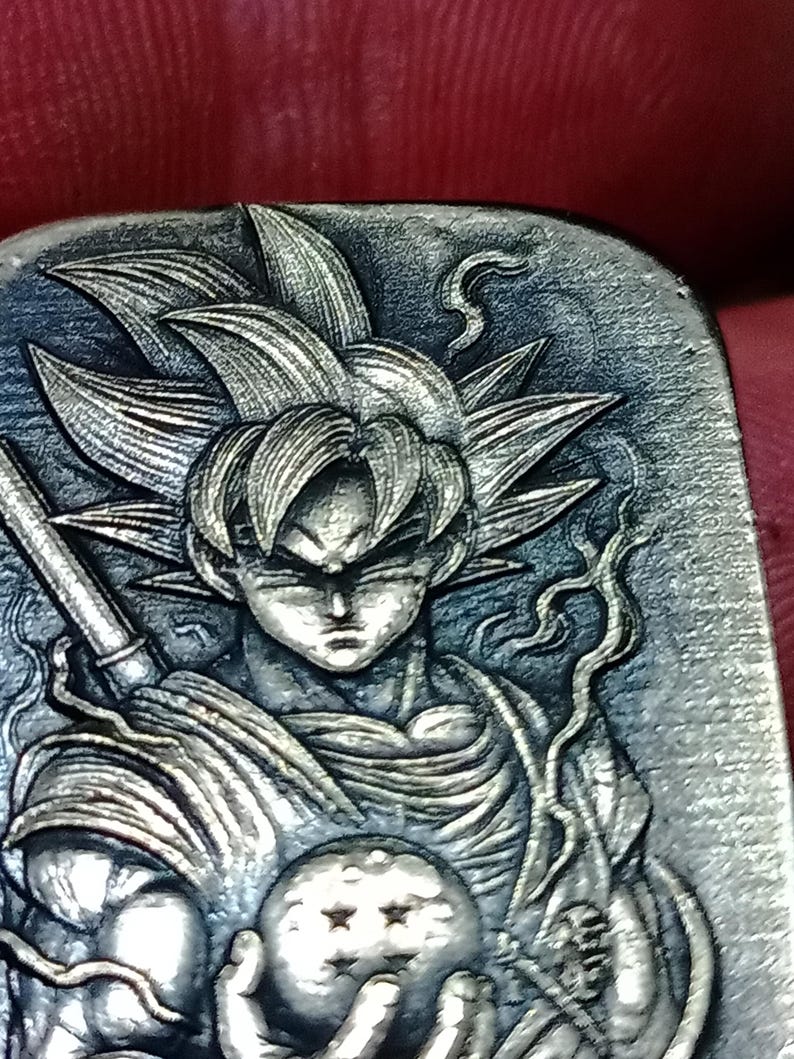 May include: A detailed, silver-toned relief carving of a character with spiky hair, holding a staff and a sphere with stars. The character's face is stern, and the artwork has intricate details.