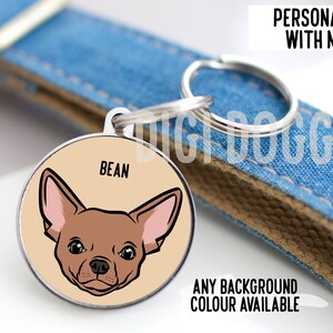 May include: A round metal pet ID tag featuring a tan background and a cartoon illustration of a brown chihuahua dog face. The name BEAN is printed in black above the dog. The tag includes a silver split ring for attachment to a blue denim collar.