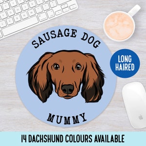 Può includere: Un tappetino per mouse rotondo blu e bianco con un'illustrazione di cartone animato di un bassotto a pelo lungo. Il testo "SAUSAGE DOG" è scritto in un semicerchio nero sopra la testa del cane. Il testo "MUMMY" è scritto sotto la testa del cane. Il testo "LONG HAIRED" è scritto in un cerchio blu nell'angolo in alto a destra del tappetino per mouse. Il testo "14 DACHSHUND COLOURS AVAILABLE" è scritto sotto il tappetino per mouse.