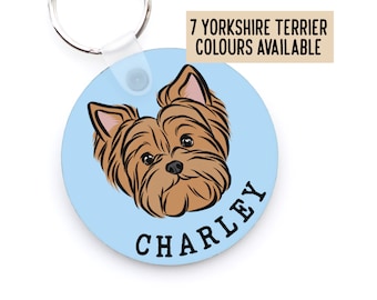 Puede incluir: Llavero redondo azul con una ilustración de perro Yorkshire Terrier de dibujos animados y el nombre "CHARLEY" impreso en texto negro. 7 colores de Yorkshire Terrier disponibles.