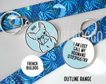 Puede incluir: Dos chapas para perros azules y blancas con anillos plateados. Una chapa tiene una ilustración en blanco y negro de un Bulldog Francés con el nombre "Hugo" en ella. La otra chapa dice "Estoy perdido llama a mis humanos 07123456789".