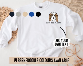 Puede incluir: Sudadera blanca con una ilustración de un perro Bernedoodle marrón y blanco y el texto "BEST DOG PARENT". El texto "ADD YOUR OWN TEXT" también está en la sudadera. Hay 14 colores de Bernedoodle disponibles.