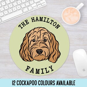 May include: A round, light green mouse mat with a brown Cockapoo dog illustration in the centre. The text "THE HAMILTON FAMILY" is printed in black around the dog's head. The text "12 COCKAPOO COLOURS AVAILABLE" is printed in black at the bottom of the mouse mat.