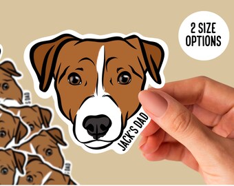 May include: A sticker featuring a Jack Russell Terrier's face with brown and white markings. The text "JACK'S DAD" is on the sticker. The image also includes the text "2 SIZE OPTIONS" and "9 JACK RUSSELL TERRIER COLOURS AVAILABLE".