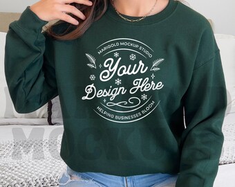 May include: A dark green sweatshirt with a white circle design that says "Marigold Mockup Studio" and "Your Design Here" with snowflakes and leaves around the text. The text below the circle says "Helping Businesses Bloom".