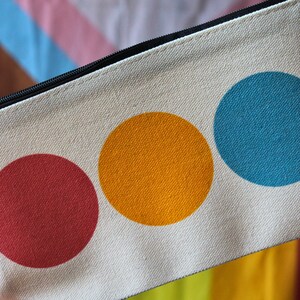 May include: A white canvas zippered pouch with three large colourful circles. The circles are red, orange, and blue.