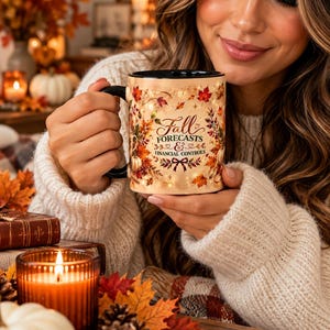 May include: A ceramic mug with a black handle and interior, featuring a cream-colored exterior decorated with autumn leaves, pumpkins, and the text Fall FORECASTS & FINANCIAL CONTROLS in brown script and block lettering.
