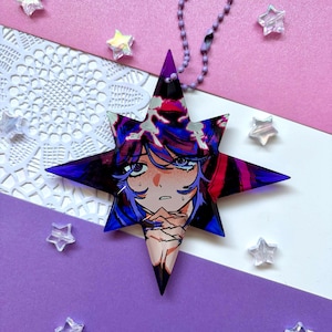 May include: A star-shaped acrylic charm featuring a colorful anime-style illustration of a character with blue hair and purple eyes. The charm has a glossy finish and is attached to a purple ball chain, showcasing vibrant shades of blue, purple, and pink.