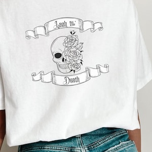 Op de afbeelding: Wit T-shirt met een zwart-witte afbeelding van een schedel met rozen en een banner met de tekst "Lash til' Death."