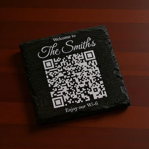 May include: A square, black slate coaster featuring a white QR code and the text "Welcome to The Smith's" and "Enjoy our Wi-fi". The coaster rests on a dark wood surface.