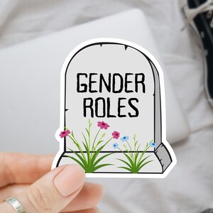 May include: A white sticker with a tombstone design that says "Gender Roles" with flowers and grass growing around it.