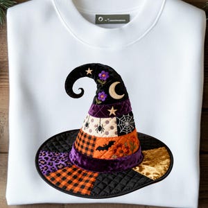 May include: A white crewneck sweatshirt featuring a large, central patch of a witch hat. The hat is constructed from various quilted fabric patterns including purple leopard print, orange and black plaid, gold velvet, and black quilted fabric.