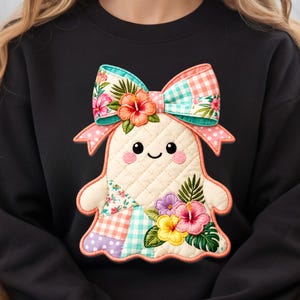 May include: A black sweatshirt featuring a quilted ghost-shaped applique. The ghost has a smiling face, pink cheeks, and is decorated with colorful floral embroidery and patchwork patterns in gingham, polka dots, and tropical hibiscus flower motifs.