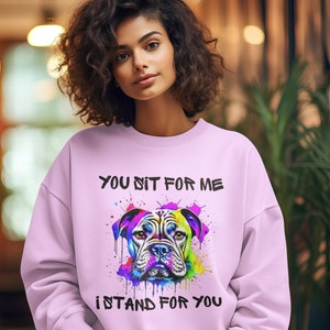 May include: A pink sweatshirt with a colourful graphic of a bulldog's head and the text "You sit for me I stand for you".