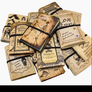 Puede incluir: Una colección de diarios de estilo vintage con cubiertas de papel envejecido, asegurados con bandas elásticas negras. Las cubiertas presentan ilustraciones de esqueletos, murciélagos y etiquetas de boticario, con textos como "Love Brew" y "Flexibility Tea".
