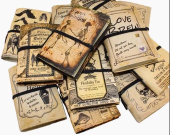 Op de afbeelding: Een verzameling vintage-achtige tijdschriften met verouderde papieren omslagen, vastgezet met zwarte elastiekjes. De omslagen tonen illustraties van skeletten, vleermuizen en apothekerslabels, met teksten als "Love Brew" en "Flexibility Tea".