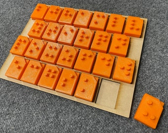 May include: A wooden board with 25 orange plastic tiles, each with a different number of raised dots. The tiles are arranged in a grid pattern. There is a single orange tile with raised dots sitting off to the side of the board.