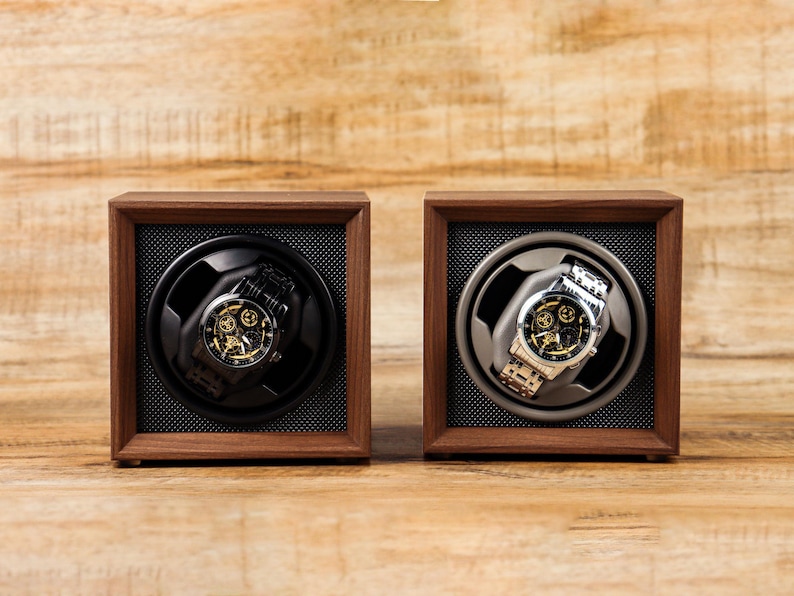 K&ouml;nnte beinhalten: Zwei Uhrenbeweger aus Holz mit einer schwarzen und silbernen Uhr im Inneren. Die Beweger sind aus dunklem Holz mit einem schwarzen und grauen Innenraum.