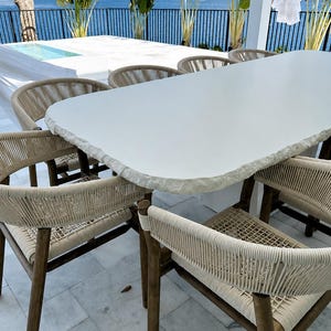 May include: A dining set featuring a large rectangular table with a thick, white, rough-hewn stone top and six chairs. Each chair has a dark wooden frame and a seat and backrest constructed from woven light beige rope in a circular pattern.