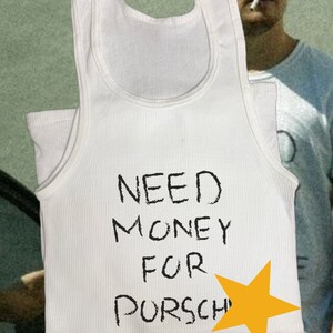 Peut inclure: Un d&eacute;bardeur blanc avec le texte "NEED MONEY FOR PORSCHE" &eacute;crit en noir. Une &eacute;toile jaune est dessin&eacute;e &agrave; c&ocirc;t&eacute; du texte.