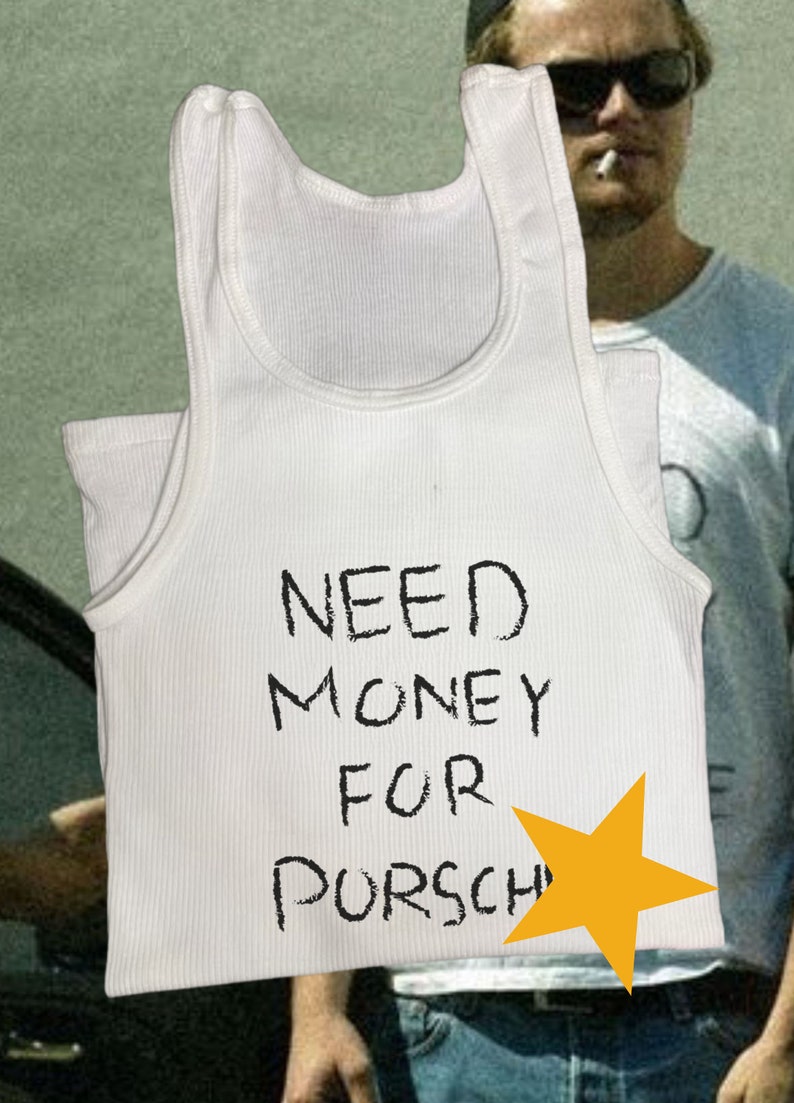 Peut inclure: Un d&eacute;bardeur blanc avec le texte "NEED MONEY FOR PORSCHE" &eacute;crit en noir. Une &eacute;toile jaune est dessin&eacute;e &agrave; c&ocirc;t&eacute; du texte.