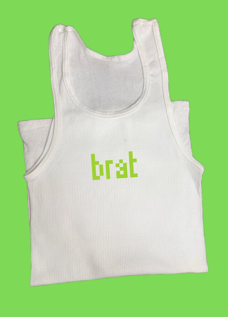 May include: White ribbed tank top with the word "brat" in green pixelated font. The top has a scoop neck and a sleeveless design. The background is a solid lime green color.
