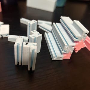 May include: A collection of small, geometric 3D-printed objects in various shapes and colors. The pieces are primarily white and light blue, with some pink accents. They appear to be components of a larger structure or model.