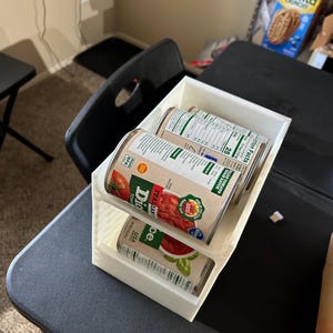 May include: A white, three-compartment organizer holding three cans of diced tomatoes and tomato sauce. The cans are labeled with the brand name and product information. The organizer sits on a black table.
