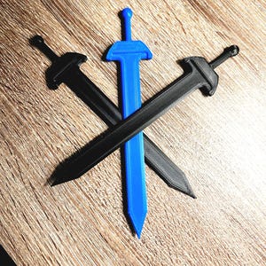 Puede incluir: Se muestran tres espadas de juguete. Una es de color azul brillante y las otras dos son negras. Las espadas están dispuestas en un patrón cruzado sobre un fondo de madera. Las espadas tienen un diseño sencillo y estilizado.