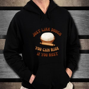 May include: Black hooded sweatshirt with the text "Just like dough you can rise if you rest" in brown lettering. A cartoon image of a ball of dough in a bowl with a rolling pin is above the text.