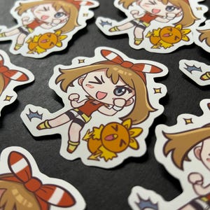 May include: A set of eight stickers featuring a cartoon character with brown hair, a red headband, and a red and white outfit. The character is holding a small, yellow, bird-like creature. The stickers are printed on white paper.