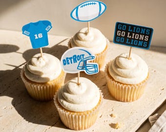 May include: Four cupcakes with white frosting, each topped with a paper topper. The toppers feature a blue jersey with the number 16, a white football, a white helmet with the text DETROIT, and a blue sign with the text GO LIONS GO LIONS GO LIONS.