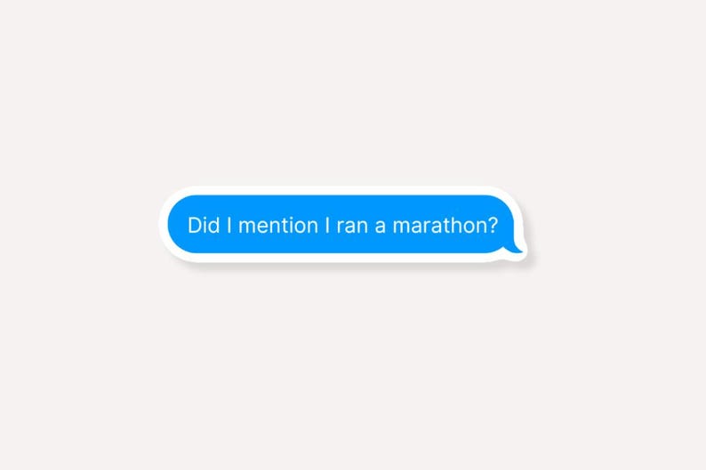 K&ouml;nnte beinhalten: Ein blauer Textblasen-Aufkleber mit dem wei&szlig;en Text "Did I mention I ran a marathon?". Der Aufkleber hat einen wei&szlig;en Rand und befindet sich vor einem hellbeigen Hintergrund.