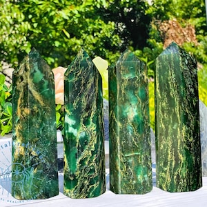 May include: Four green and gold serpentine stone points, also known as green aventurine, are arranged in a row on a white surface. The points are all approximately the same size and shape, and they have a smooth, polished finish.