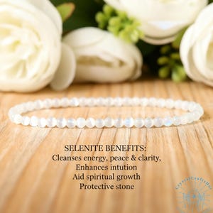 May include: A delicate white selenite bracelet composed of small, round beads. The bracelet is displayed on a wooden surface, with white flowers in the background. Text on the image lists selenite benefits: Cleanses energy, peace & clarity, Enhances intuition, Aid spiritual growth, Protective stone.