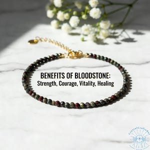 May include: A beaded bloodstone bracelet with a gold-colored chain and clasp. The bracelet features small, round beads in shades of green and red. Text on the image reads: BENEFITS OF BLOODSTONE: Strength, Courage, Vitality, Healing.